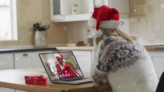 在笔记本电脑视频通话中，雪花落在圣诞老人帽子上的快乐高加索女人身上的动画