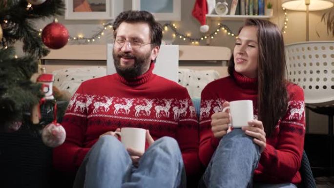 圣诞节，新年，前夜。幸福的夫妻男人和女人坐在地板上，看着圣诞树，喝茶和聊天。慢动作