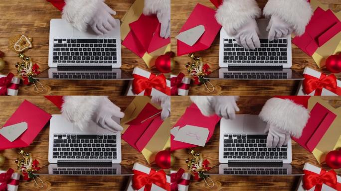 顶视图圣诞老人戴着白手套的手在木制新年装饰桌子上的键盘笔记本电脑上打字。圣诞老人浏览孩子们的来信，并