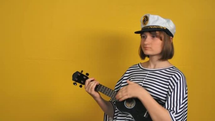 年轻的金发女孩在黄色背景的工作室里弹尤克里里吉他