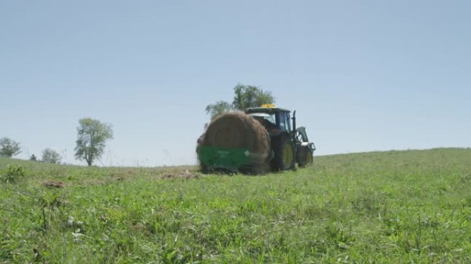一位农民将一捆干草从拖拉机上展开到田地中
