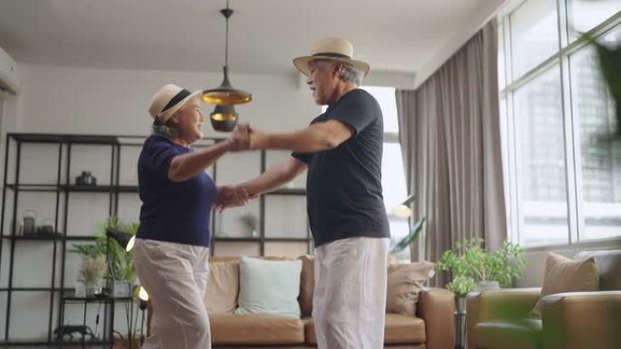 幸福退休的亚洲爱情夫妇退休的老年夫妇在家，亚洲老年人一起跳舞笑着在家里的客厅欢快的微笑检疫呆在家里锁