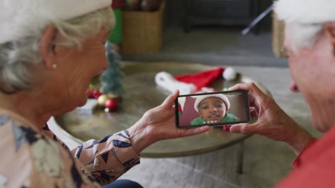 微笑的白人高级夫妇使用智能手机与屏幕上的男孩进行圣诞节视频通话