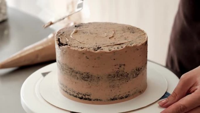 4k女糕点厨师在巧克力蛋糕上抚平巧克力奶油，特写镜头。慢动作。蛋糕制作过程。