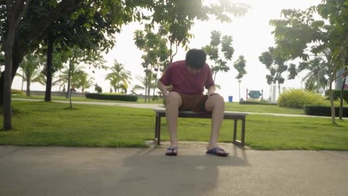 亚洲青春期男孩坐在公园的户外长凳上，以太阳光为背景，生活方式为概念。