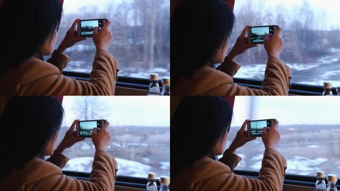 亚洲妇女穿着棕色外套独自旅行，并通过火车运输与手机合影，并通过窗户看着风景