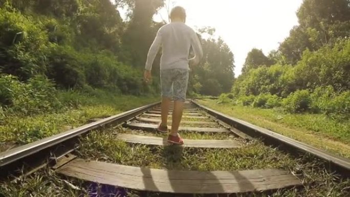 慢镜头男孩沿着铁路走，在两边郁郁葱葱的绿色植被中踏着宽阔的台阶