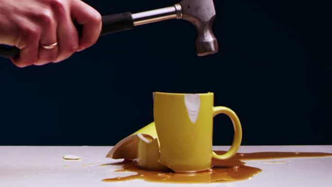 男人的手用铁锤打碎了一个带有液体的黄色茶杯