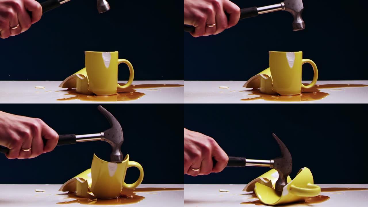男人的手用铁锤打碎了一个带有液体的黄色茶杯