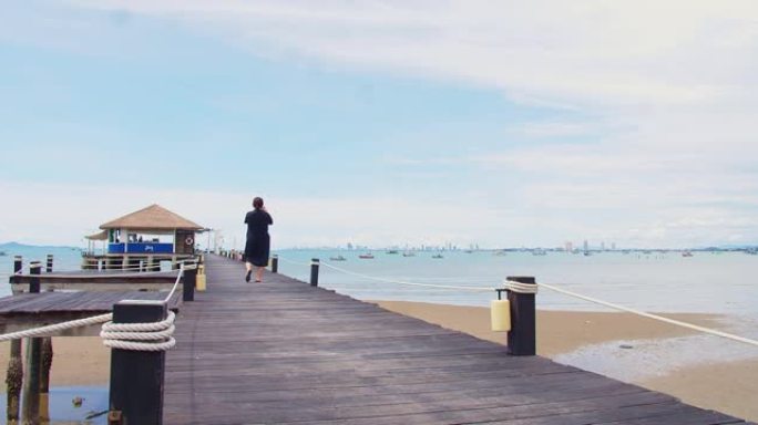 女人在阳光明媚的日子里，在海边的木制码头上散步拍照，在泰国芭堤雅乘坐蓝天船，在度假和旅行中放松