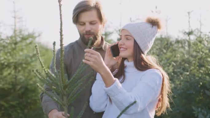 一对好看的积极幸运的年轻夫妇的特写镜头，他们在特殊的地方购买了枞树，种植了枞树，女人在手机上聊天