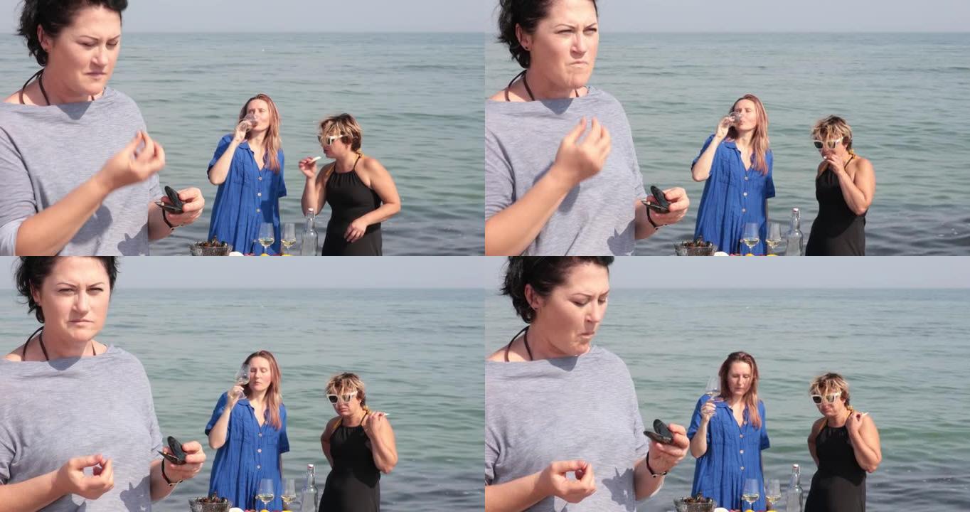 女人从贝壳上拿贻贝吃东西，而女人在海边喝酒