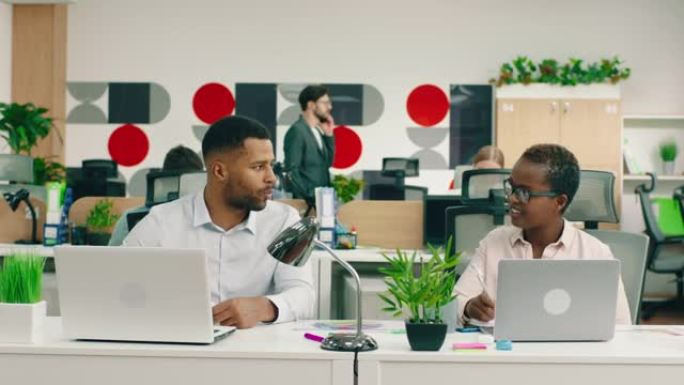 两名极具吸引力的非洲工人在一间灯火通明的大办公室里，他们在餐桌旁互相帮助工作和交谈。阿里·阿列克谢迷