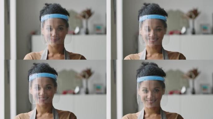 漂亮的非洲裔美国妇女戴着保护性塑料面具看着相机，微笑着。年轻的女性混血在灯光室的背景下摆姿势。特写。