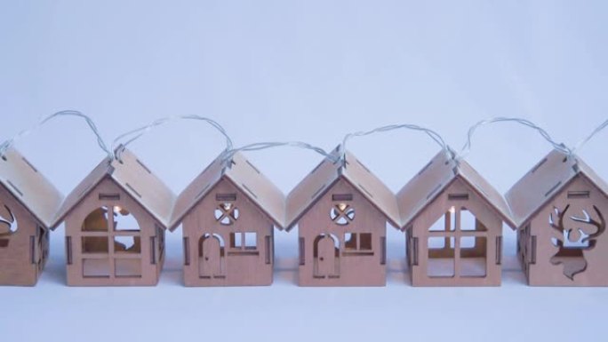 木制玩具屋排成一排。房子里的花环和灯亮着。电的出现的概念。圣诞节假期用照明装饰房屋的概念
