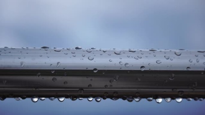 在模糊的海洋背景下，不锈钢扶手上的雨滴。特写镜头。雨露中的水滴聚集在闪亮的钢铬杆手轨栏杆上