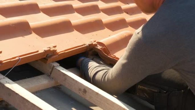 工人手的特写镜头安装黄色陶瓷屋面瓦，安装在覆盖在建住宅屋顶的木板上。