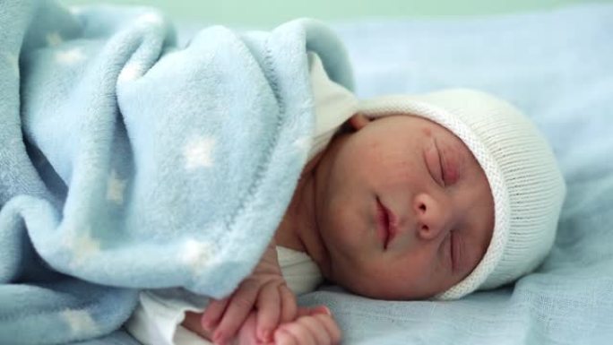 初生婴儿脸部肖像的特写镜头早年在白色蓝色背景上甜蜜地睡觉。孩子在帽子上生命的开始。婴儿，分娩，出生的
