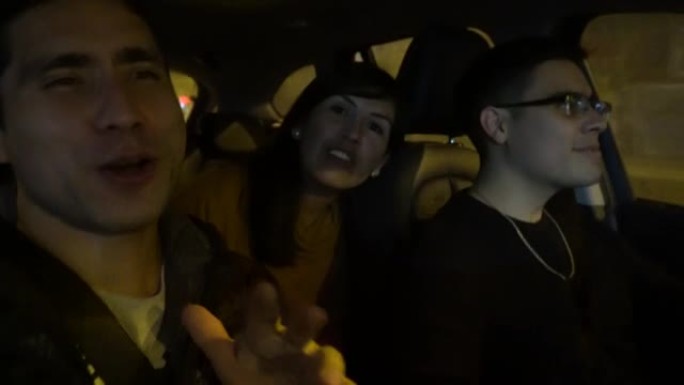 三个朋友的自拍照在夜间外出时在行驶中的汽车中唱歌和开车，看着相机做手势，微笑和交谈