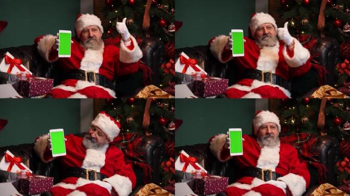 圣诞老人躺在装饰过的圣诞树附近的沙发上，并展示了一个带有绿屏chrome键的平板电脑，同时做了一个竖