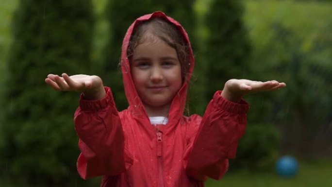 快乐的小女孩在雨中微笑。孩子热爱自然，幸福自由。玩水滴雨的孩子。儿童在下雨的夏日在户外玩耍。穿着红色