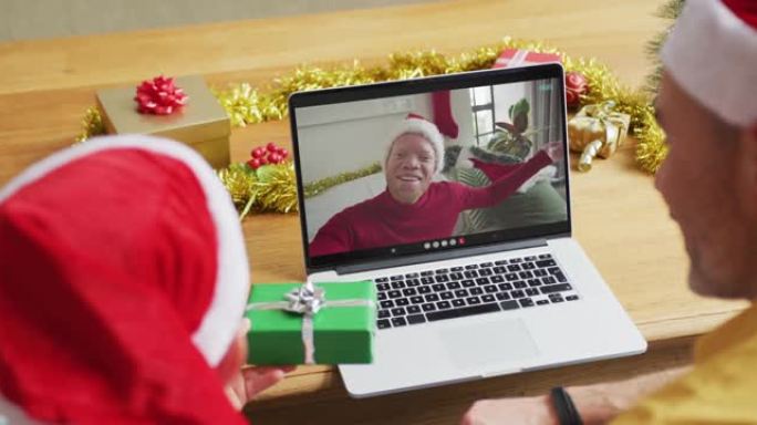 白人父亲和儿子戴着圣诞老人的帽子，使用笔记本电脑与屏幕上的男人进行圣诞节视频通话