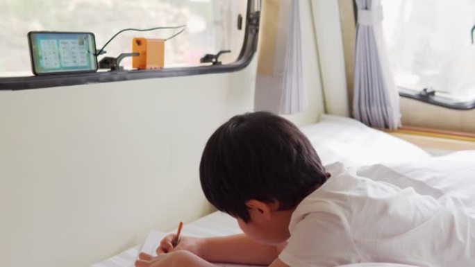 亚洲男孩正在一辆露营车上在线教室，窗外可以看到风景。范生活