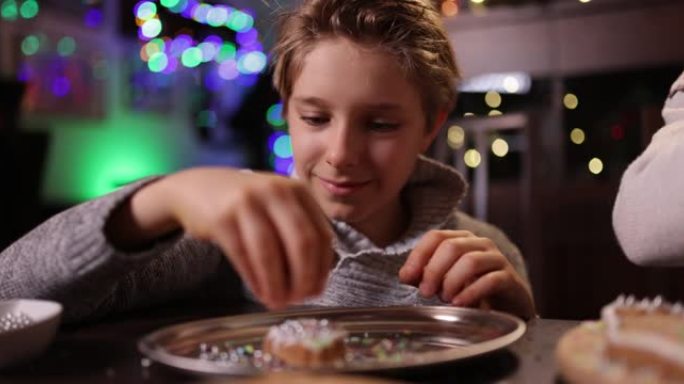 小男孩正在用糖霜，珠子和洒水装饰圣诞节姜饼屋。