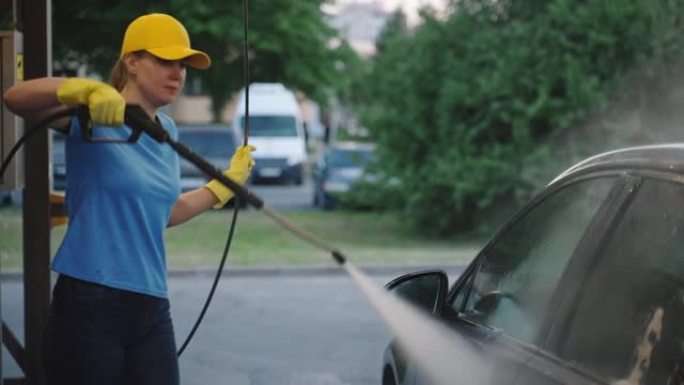 女人在统一的清洁车上使用高压水。洗车服务。