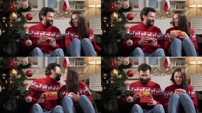 送圣诞礼物。幸福的夫妻男人和女人坐在圣诞树附近的地板上，互相送礼物。慢动作