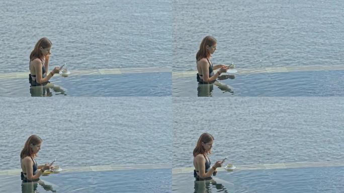 游泳池里的女人使用智能手机。海洋背景上的巴厘岛度假胜地的女性上网