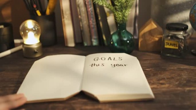 今年用手打开带目标的笔记本手写文字在家里的木头桌子上，早晨从窗户上晒出阳光。新年决议目标列表