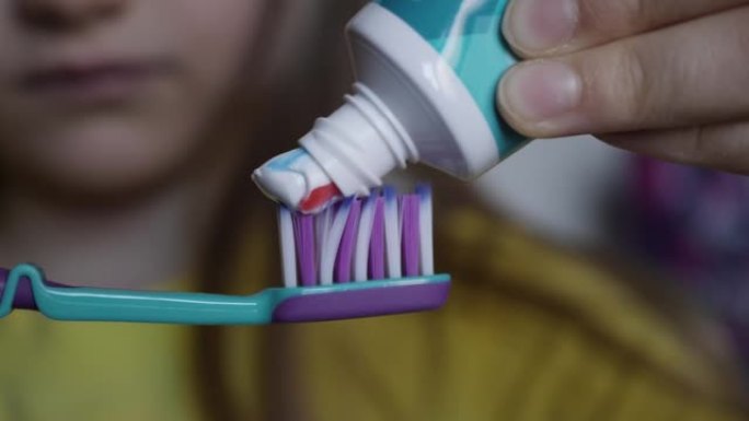 小女孩用明亮条纹牙膏挤压牙刷。宏观拍摄红色和蓝色条纹牙膏挤压儿童牙刷特写。牙齿健康口腔卫生。早上刷牙