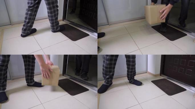 一个穿着拖鞋和睡衣的男人打开前门，拿起一个大纸箱。