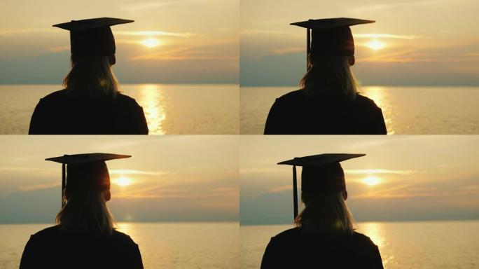 一个穿着毕业长袍和帽子的女人看着海上的日出