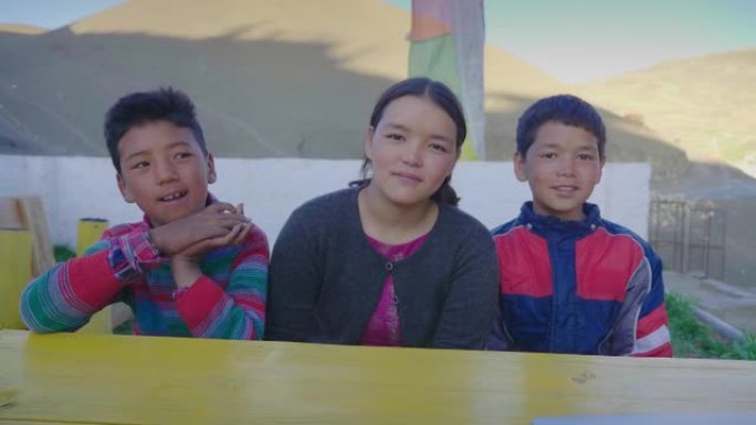 在山区寒冷地区，三个年轻的东亚孩子一起坐在户外的长凳上