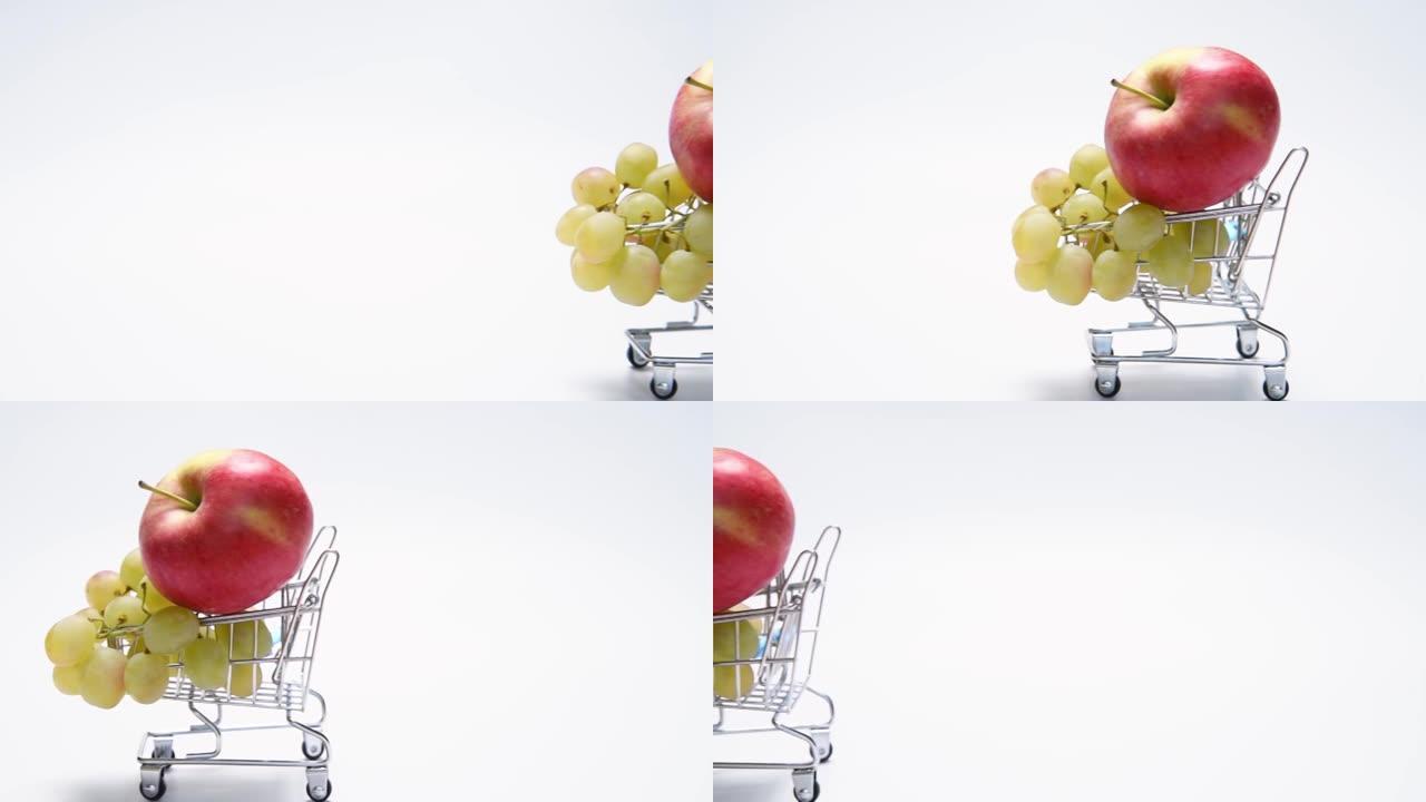 白色背景迷你购物车中的红苹果和绿葡萄。水果传递概念。循环