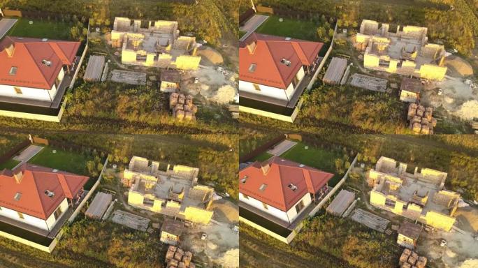 两座私人房屋的俯视图，其中一座正在建造中，带有木制屋顶框架，另一座带有红色瓷砖屋顶。
