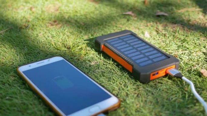 草坪上带有太阳能电池板的可充电移动电源组。连接到手机、平板电脑或智能手机并为其充电。带USB充电器的