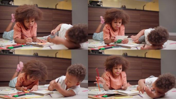 两个可爱的混血儿孩子躺在家里的地板上，用记事本的铅笔画画。富有创造力的跨种族兄弟姐妹，小女孩和她蹒跚