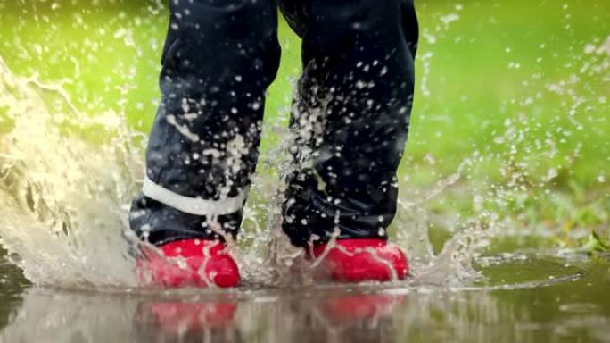 穿着红色橡胶靴的孩子在雨水坑里跳。防水服装