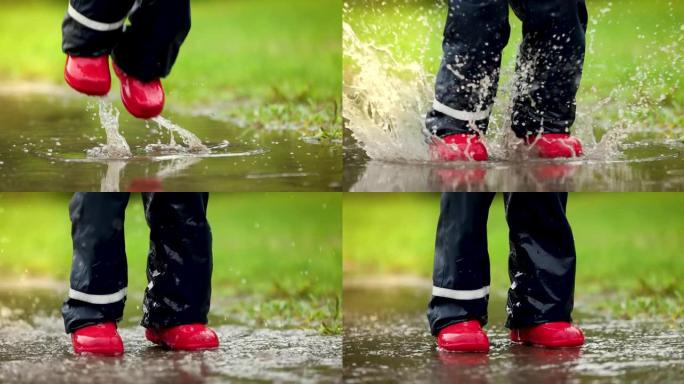 穿着红色橡胶靴的孩子在雨水坑里跳。防水服装