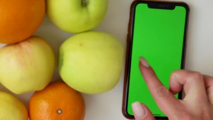 绿屏的手机躺在水果的侧面，手用手指在屏幕上发出咔嗒声和滑动