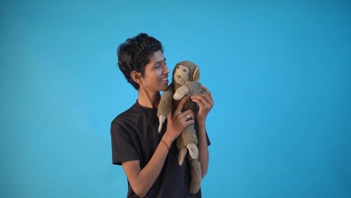 微笑的年轻印度木偶少年与他的木偶猴子在蓝色背景放松