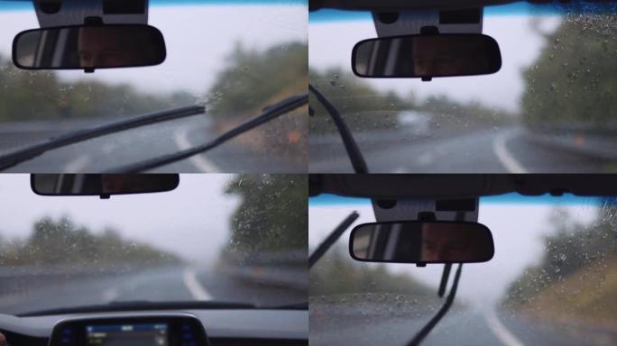 中年男子在驾驶汽车内部的镜子中的反射，在大雨中，驾驶员在公路旅行中握着方向盘并与无法识别的乘客交谈的