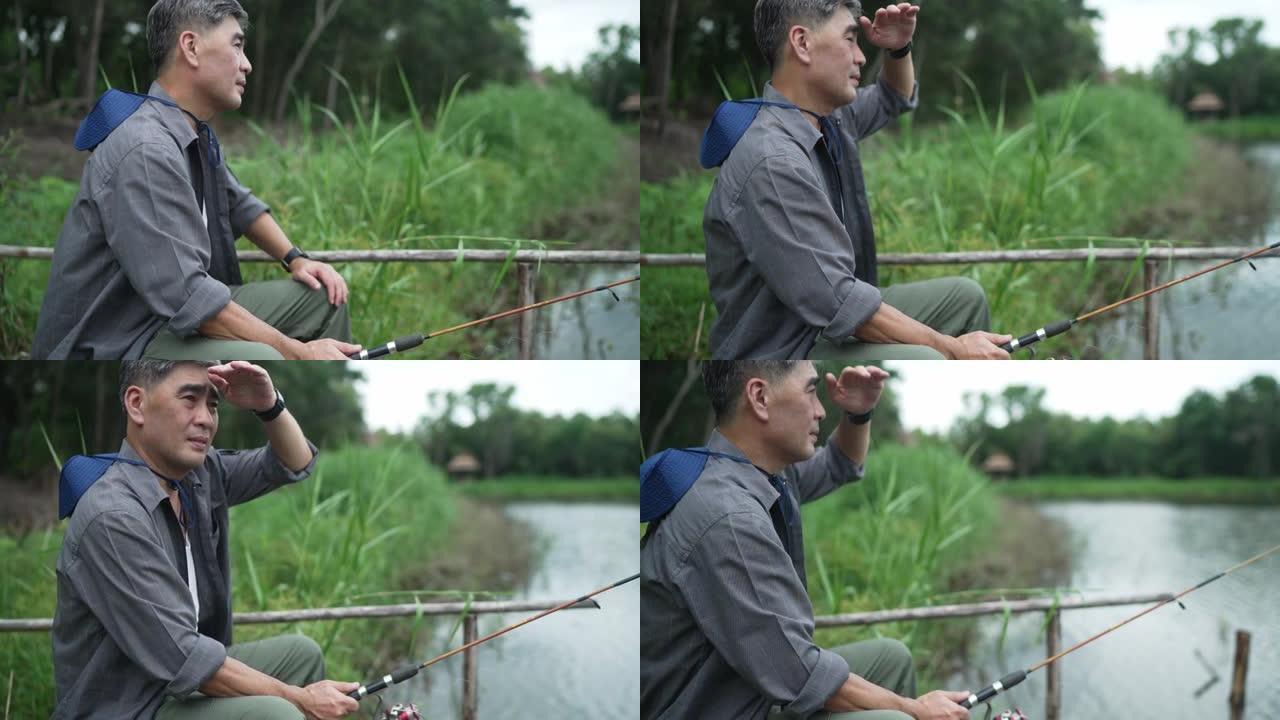 亚洲老人，白发，帽子，拿着钓鱼竿，坐在湖边钓鱼，度假，退休，老年人的爱好，概念