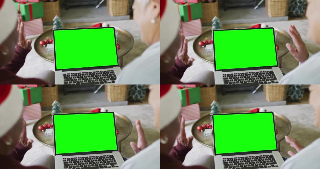 戴着圣诞老人帽子的高级多样化夫妇用绿色屏幕拨打笔记本电脑圣诞视频通话