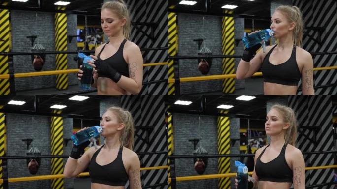 一个女孩在拳击训练中站在拳击场上喝水。