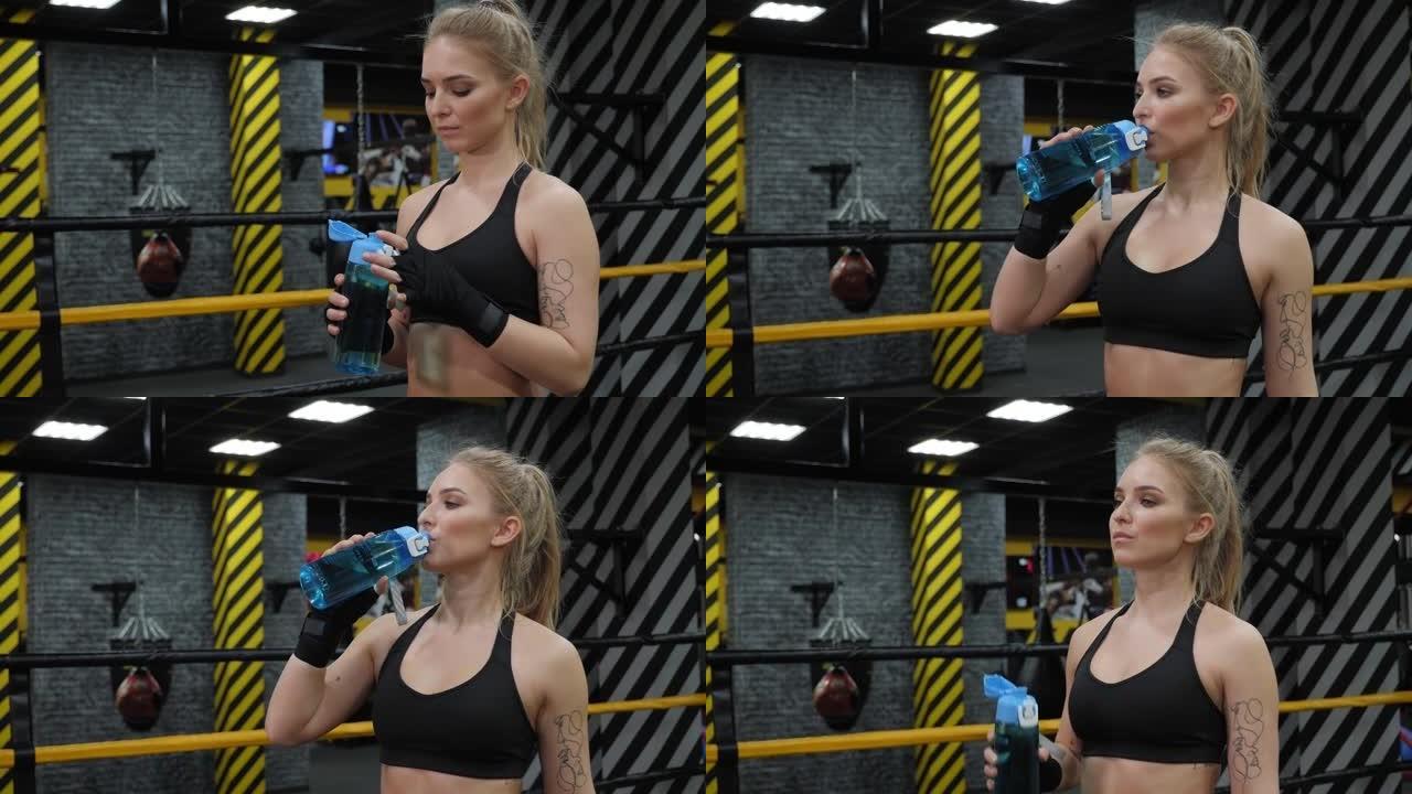 一个女孩在拳击训练中站在拳击场上喝水。