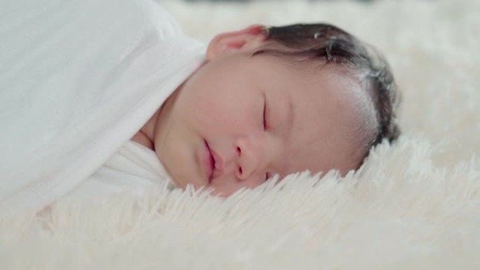 睡在白色毯子下的可爱宝宝。